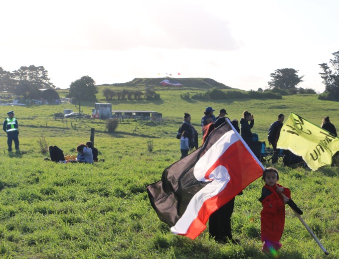 A girl with her mother holds Tino Rangatiratanga – the Māori flag of independence at Ihumātao. Image: Michael Andrew/PMC